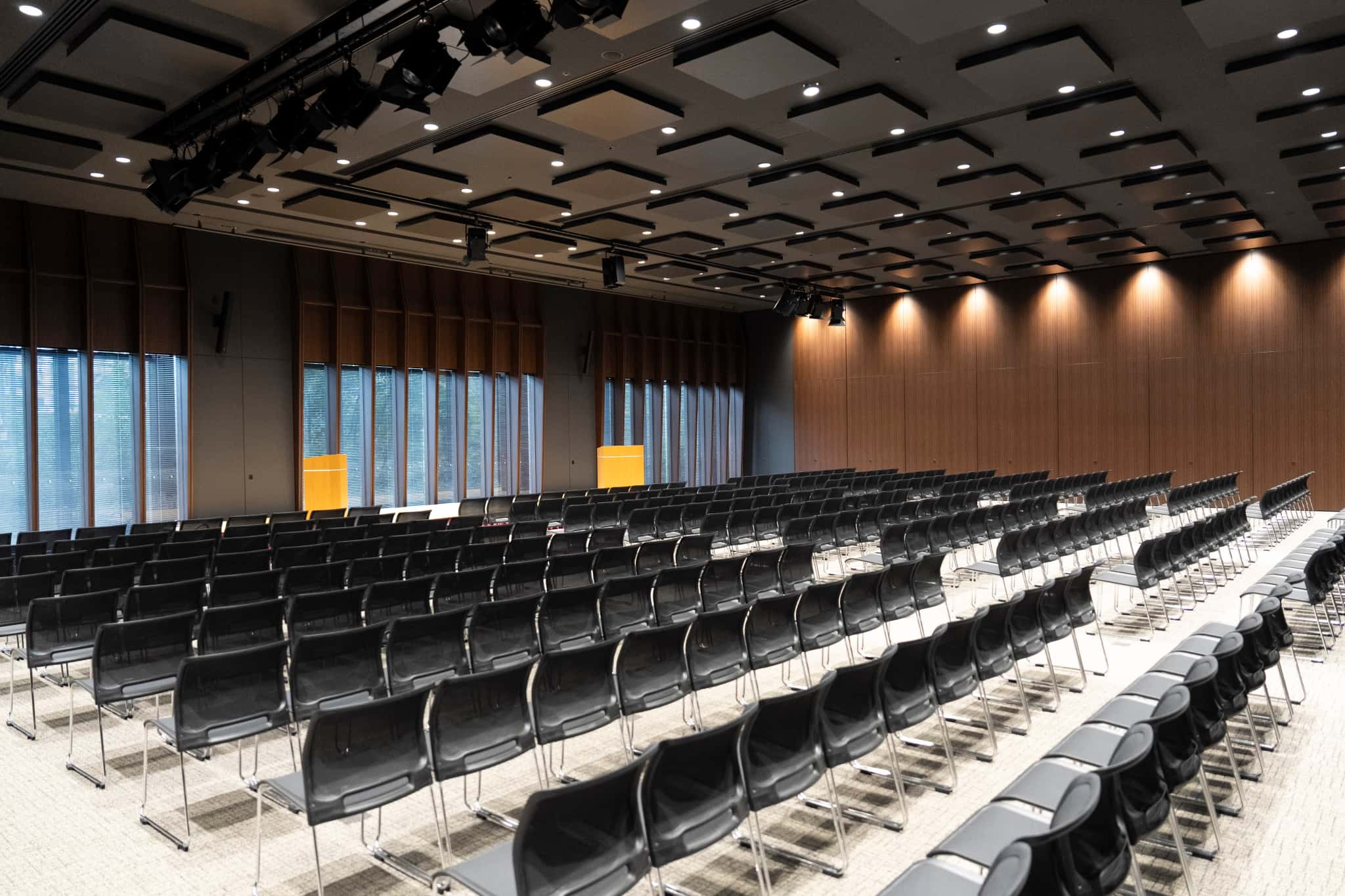 大手町プレイス ホール＆カンファレンスの建物外観のローアングルビュー。ガラス張りの高層ビルと張り出した中層部を白い円柱列が支えており、建物入口前の広場には緑豊かな植栽と案内板が設置されている。